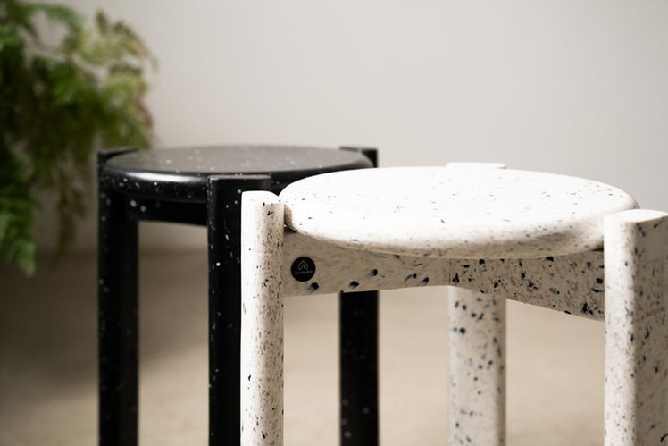 Banquinho Teco preto e banquinho Teco branco mesclado lado a lado, em ambiente interno com parede clara ao fundo