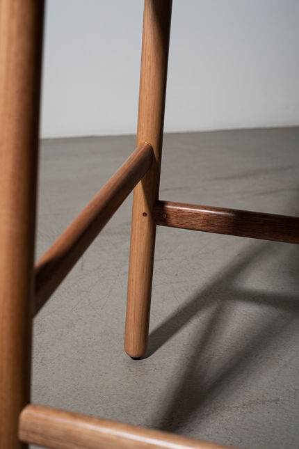 Detail of the turned solid wood legs and cross stretchers of the Hi Counter Stool on a concrete floor