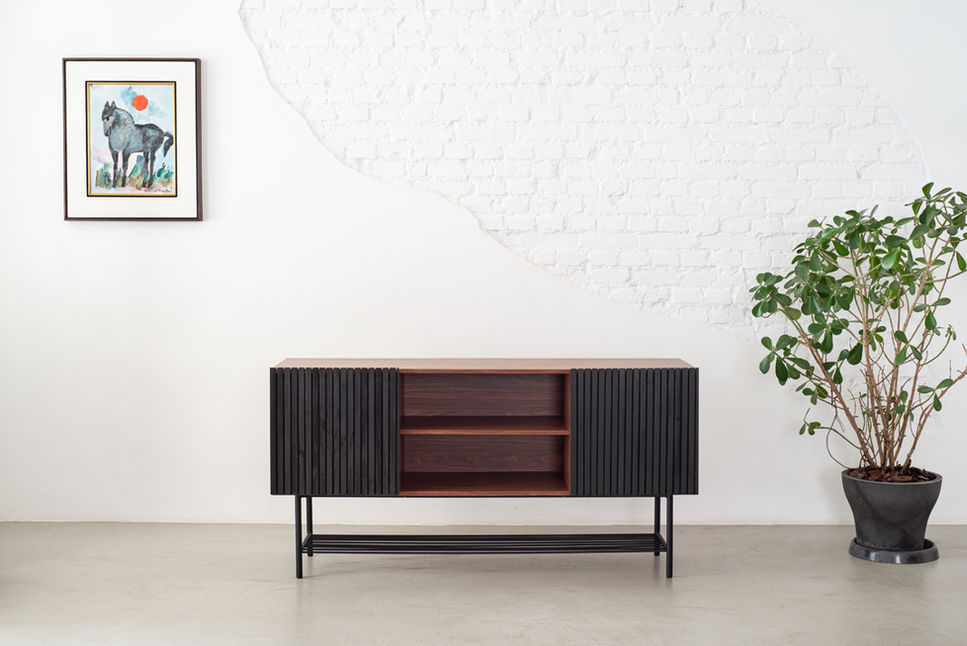 Front view of the Zero Credenza showing the two black slatted doors flanking open walnut shelving, with a potted tree alongside