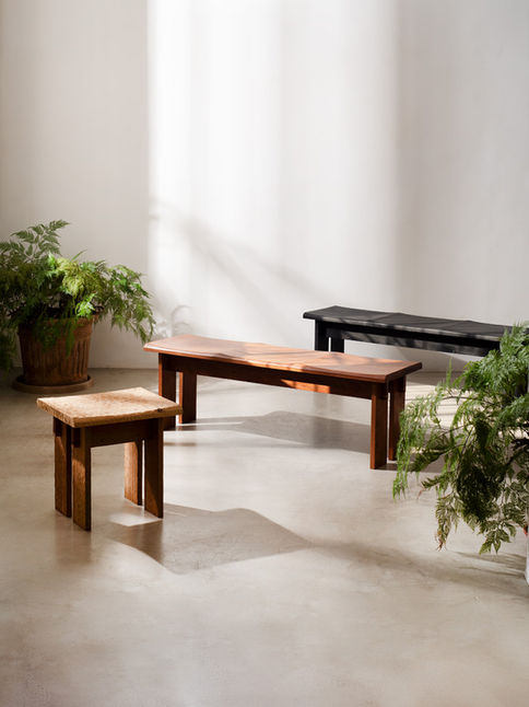 Guama Stool in the foreground next to two longer Guamá benches, beside ferns in a bright room