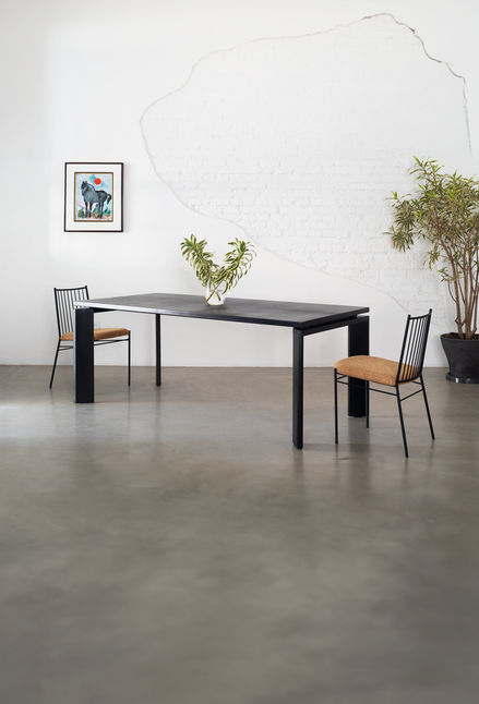 Berlin Table in black with two chairs and a glass vase, photographed in a bright concrete room