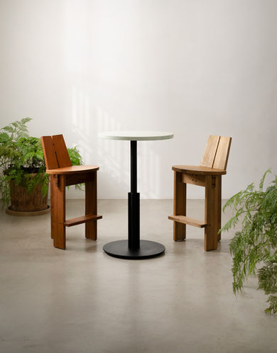 Banqueta Guamá em madeira maciça ao lado de mesa alta redonda preta, ambiente minimalista