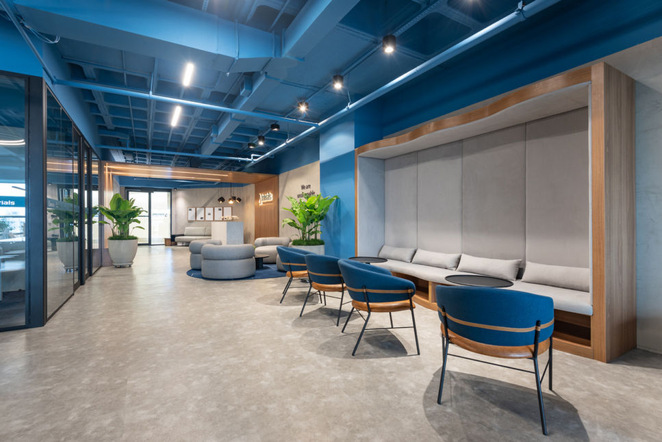Corporate lounge with several blue Oliva Lounge Chairs beside a built-in bench and blue ceiling
