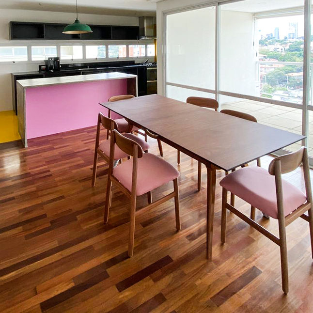Set of Hi Chairs in light solid wood with pink seats around a wooden dining table in an apartment with a pink kitchen island