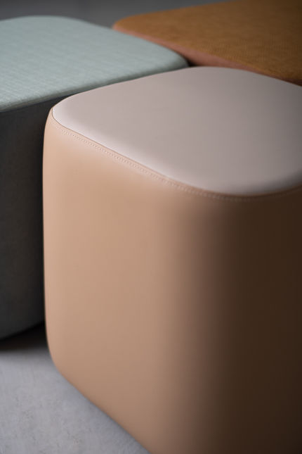 Detail of a blush Composé Ottoman with sage green and mustard pieces behind it, highlighting the seam around the seat top