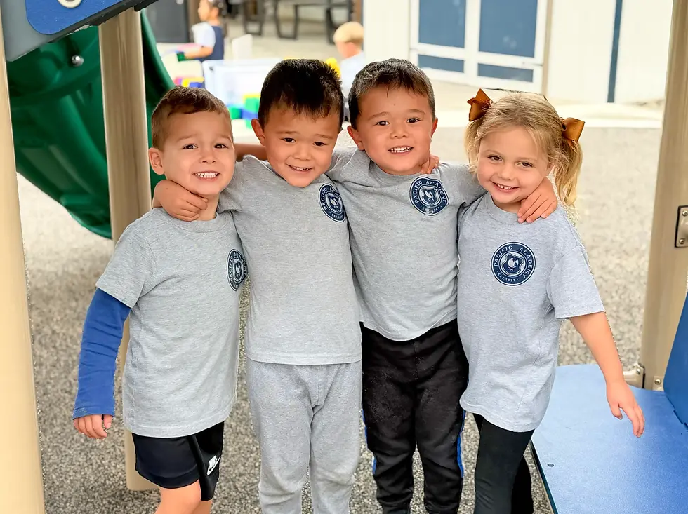 Four young children in gray "Pacific Academy" shirts smiling and hugging under playground equipment. Bright, joyful setting.