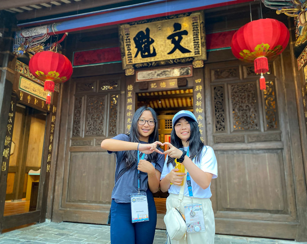 Two smiling people form a heart shape with their hands. They're standing in front of an ornate wooden building adorned with red lanterns and Chinese characters.
