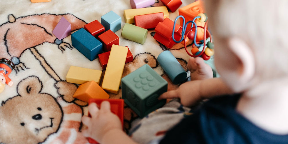 Baby playing with colorful toy blocks on a teddy bear-patterned blanket. Bright reds, blues, and yellows create a playful mood.