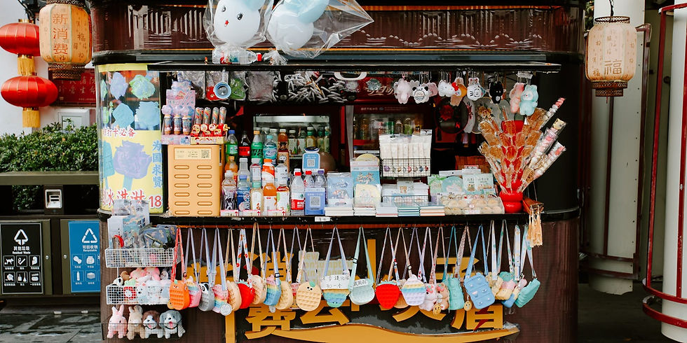 Street kiosk selling drinks, snacks, and plush toys with colorful bags hanging. Red lanterns and text signs decorate the background.