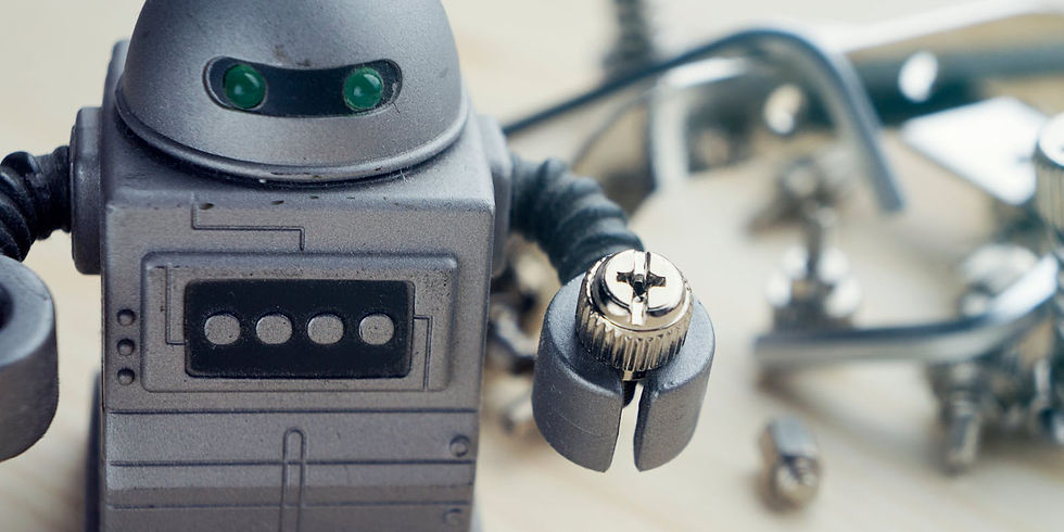Toy robot holding a screw stands on a light surface. Background shows scattered metal parts, creating a tinkering or workshop vibe.