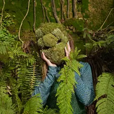 Artist Beccy McCray wearing a moss mask in Fairlight, Hastings, East Sussex