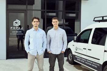 Two men posing outside POPAJ headquarters near their branded van and building
