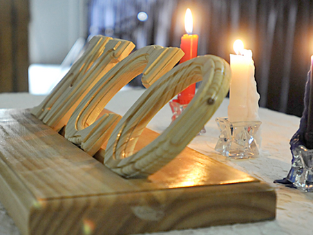 Wooden "NCO" sign on a table with three lit candles in red, white, and blue glass holders. Soft, warm lighting creates a cozy ambiance.