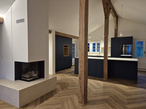 Offenes Wohnzimmer mit moderner, dunklen Küche, Kochinsel und Cheminée