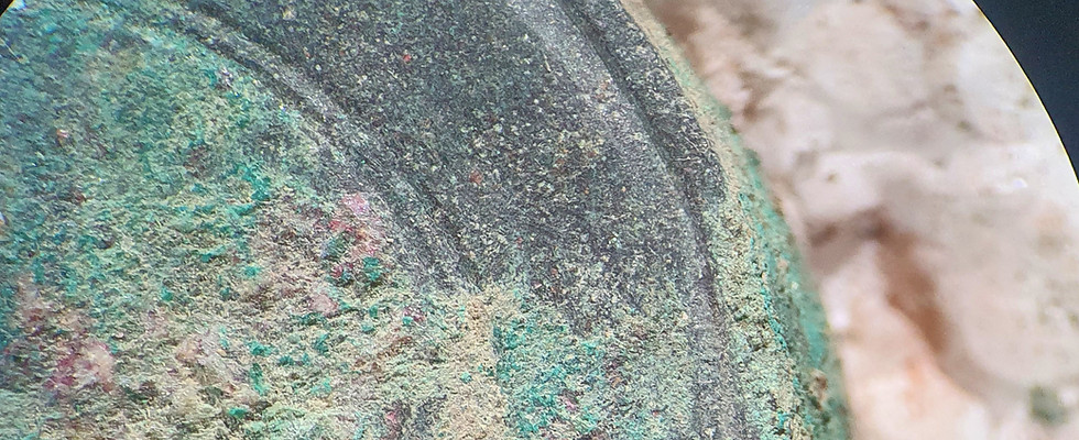 Photographie d'un objet en bronze en cours de dégagement. Une partie du métal est visible, l'autre couverte de corrosion