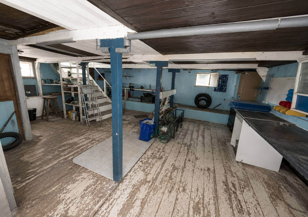 Spacious workshop or storage room with blue walls, worn wooden floors, workbench, and staircase.