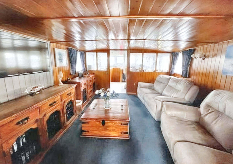 Reverse view of the houseboat lounge showing two sofas, polished wood ceiling panels, and built-in wooden cabinets.