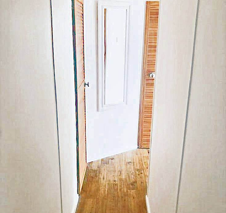 Narrow hallway inside the floating home with white walls, wood flooring, and doorways leading to cabins.
