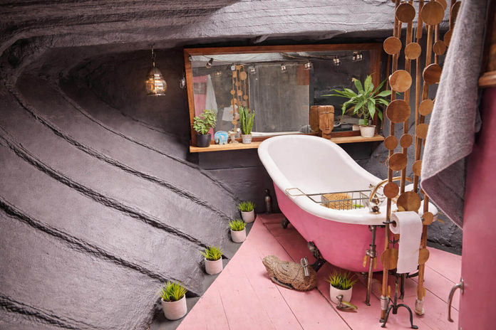Bathroom with pink clawfoot tub, wavy gray walls, and plants
