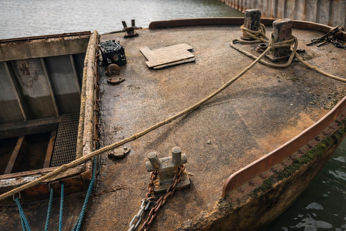 Boat detail with ropes and chains; concrete barge in water.
