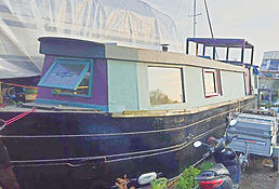 Wolfie colorful narrowboat docked for repairs, with a light blue and purple cabin, windows, and a dark hull.