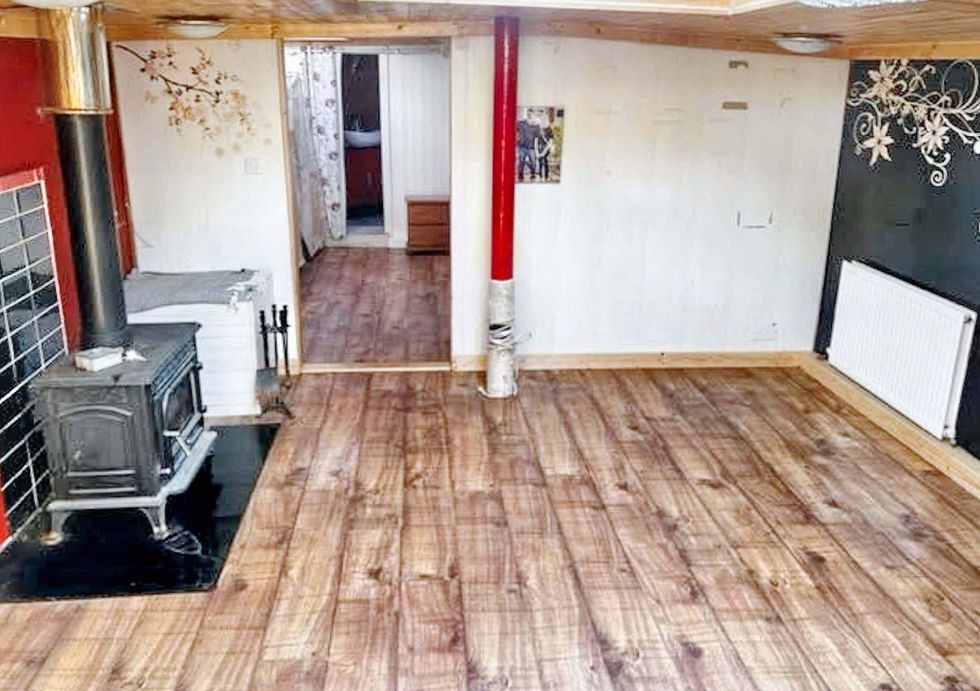 An empty room with wood-look laminate flooring, a black wood-burning stove on red wall, and a bathroom entrance.