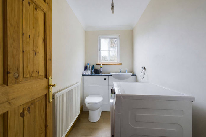 Small utility room with toilet, sink, washing machine, and wooden door