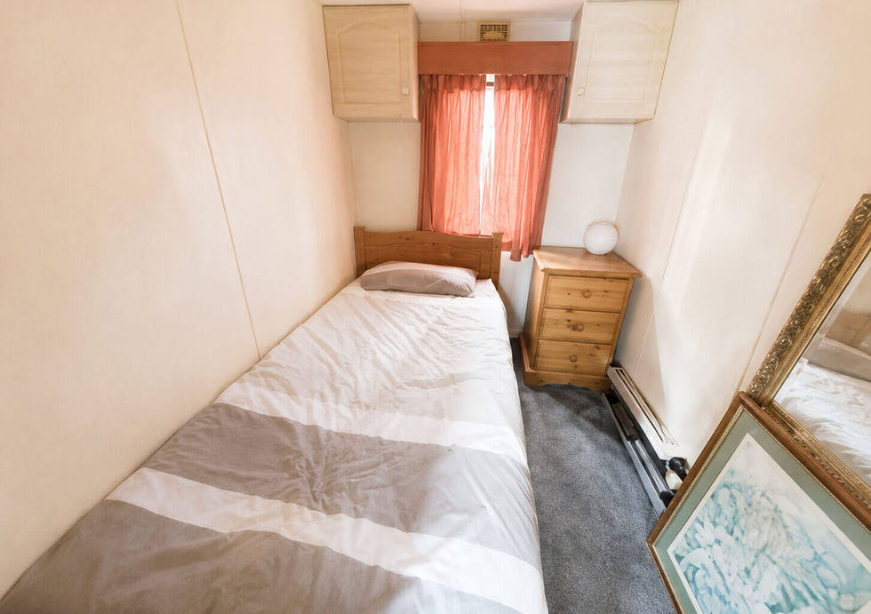 Small, cozy bedroom with a single bed with striped duvet, wooden nightstand, and orange curtains.