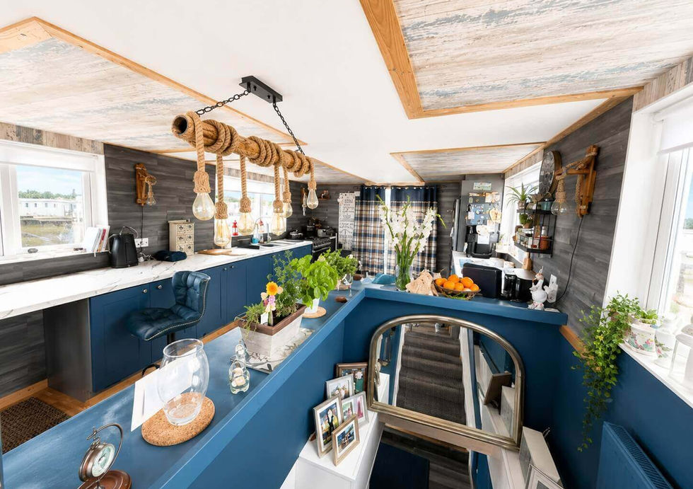 Coastal houseboat interior featuring a modern kitchen with navy blue cabinets, rope pendant lights, and a staircase.