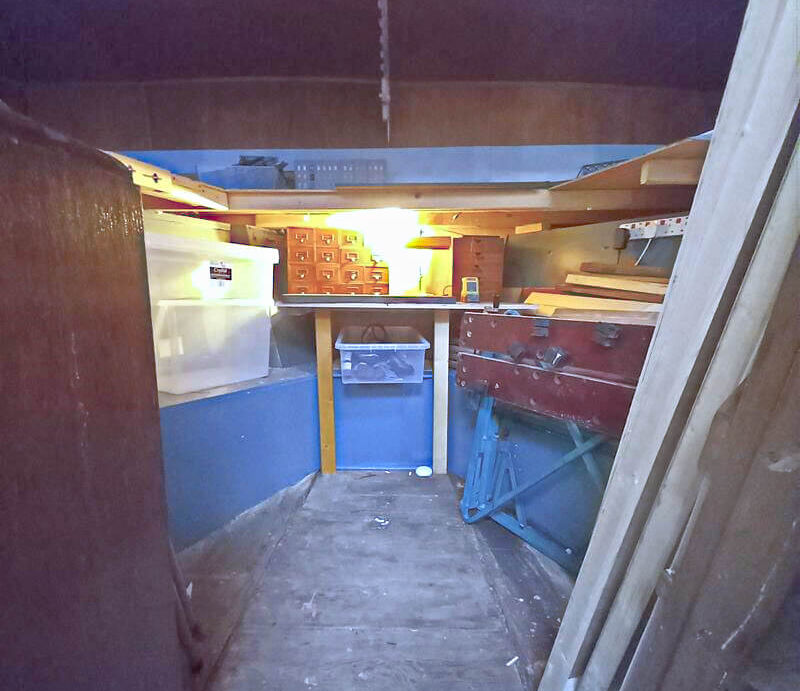 Interior of a small room with blue walls, wooden planks, storage boxes, and stacked lumber.
