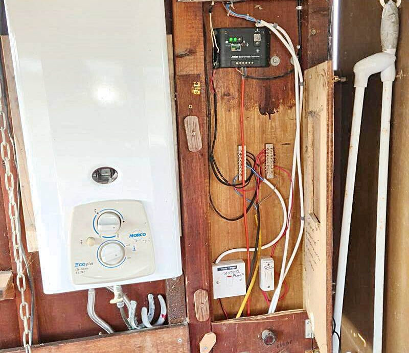 A white Morco Eco Plus water heater next to a solar charge controller and a water pump control on a wooden wall.