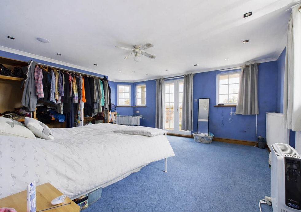 Spacious blue bedroom with a large bed, open closet, and French doors. Natural light fills the room, creating a cozy atmosphere.