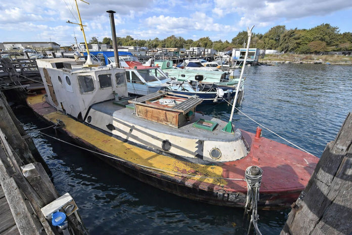 Old yellow and red workboat docked by a wooden pier.