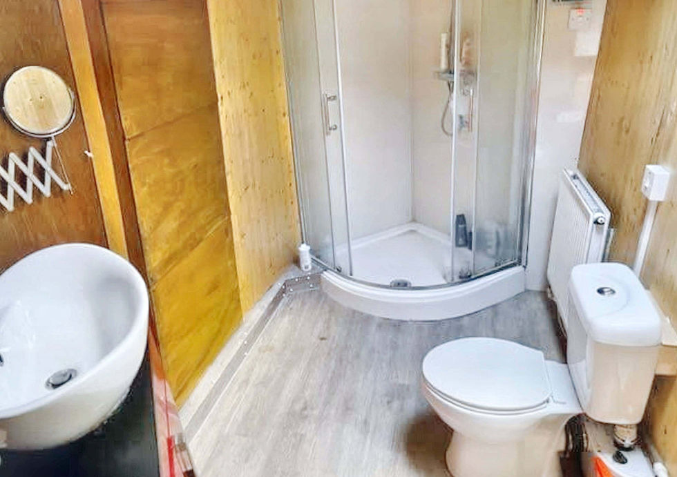 A compact bathroom with light wood paneling, a white toilet, corner shower, and small vanity sink.