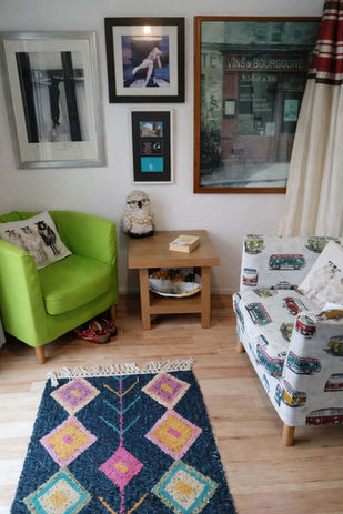 Cozy living room with green armchair, patterned sofa, geometric rug.