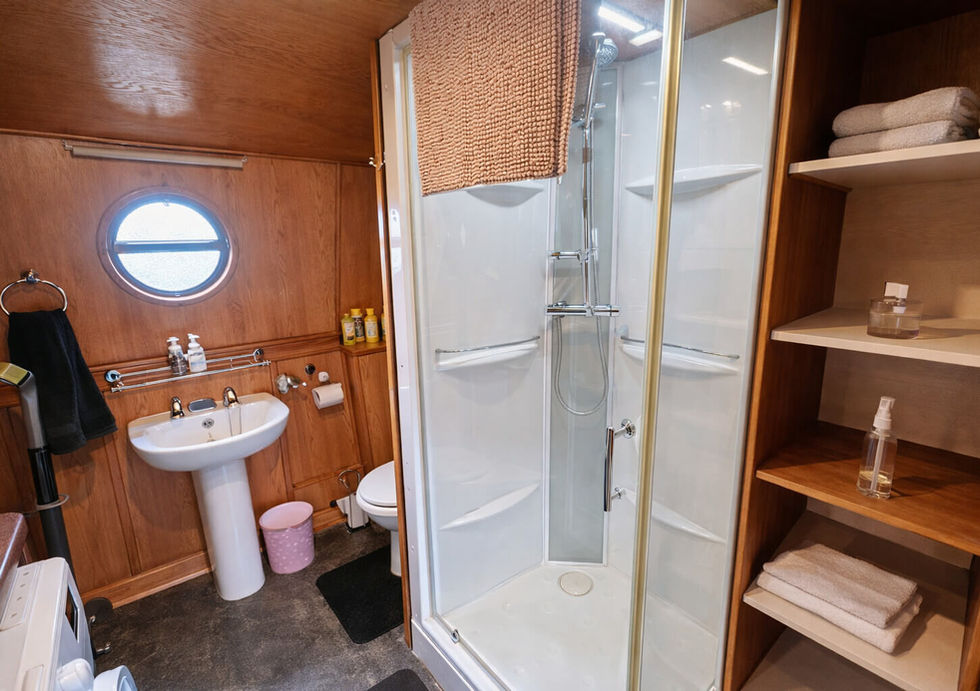 Compact bathroom with enclosed shower, shelving, pedestal sink, and circular porthole window.