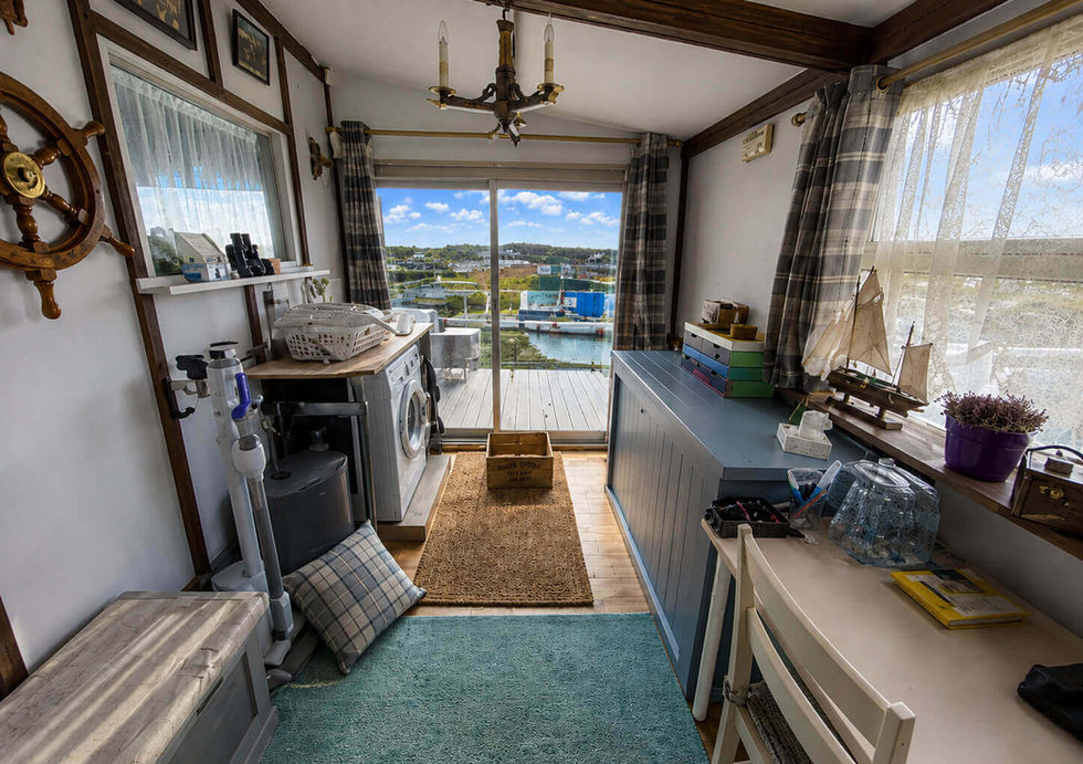 Bright, cozy laundry room with a washing machine, nautical decor, a desk, and large windows overlooking a harbor.