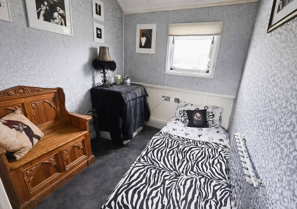 Small guest bedroom with zebra-pattern bedding, carved wooden bench, framed photographs, and patterned wallpaper.