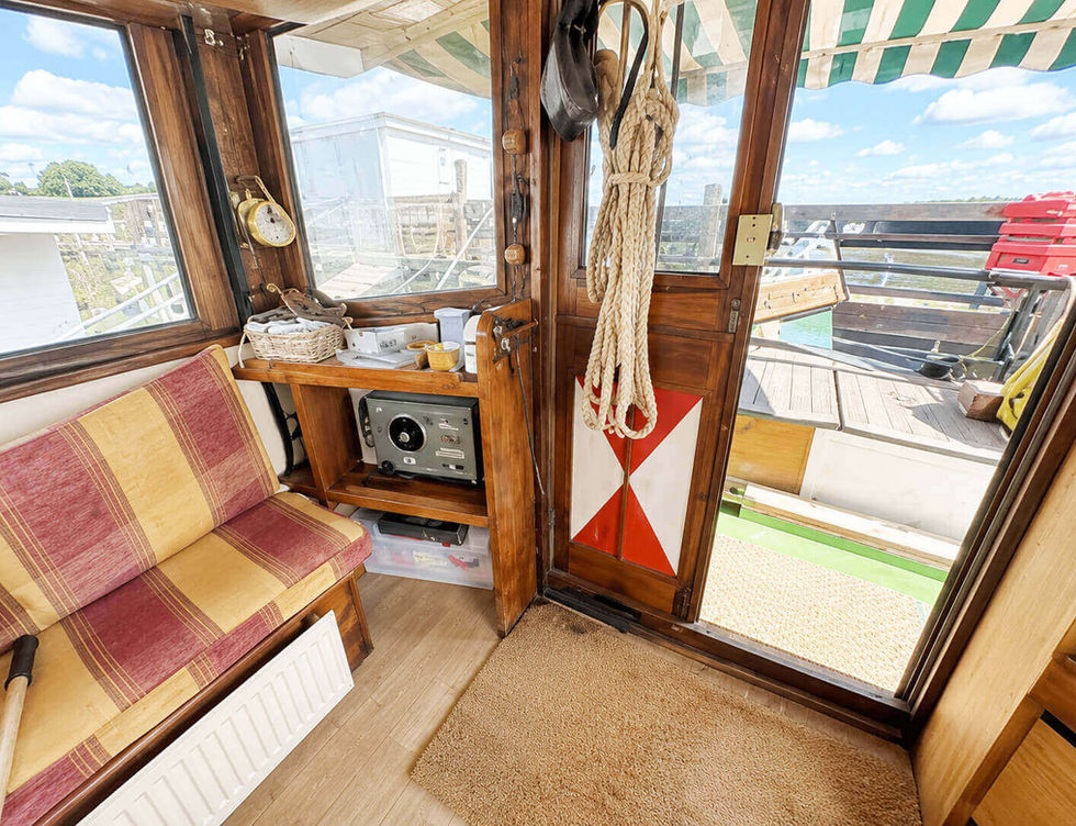 Cozy boat interior with wooden accents, striped bench, marine radio, and an open door to the deck.