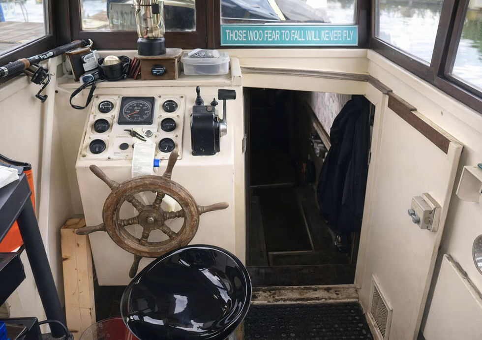 Boat cockpit with a wooden steering wheel, control panel, fishing rod, and a quote sign.