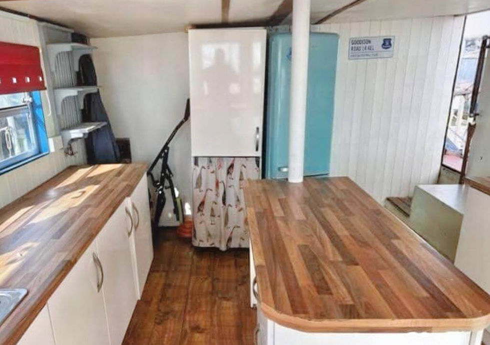 Narrowboat interior with modern white kitchen cabinets, butcher block countertops, white and blue retro fridges.