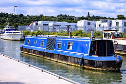 Rosa a blue and black narrowboat docked in a canal next to a white speed boat and RV storage area.