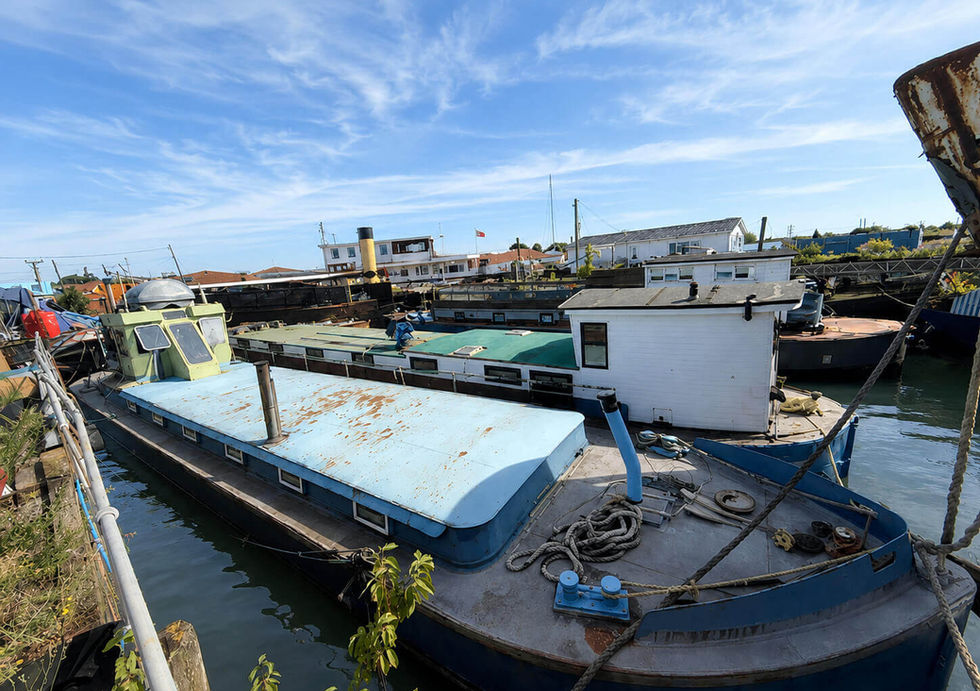 Wide view of project houseboat with spacious deck and water between boats at residential marina.