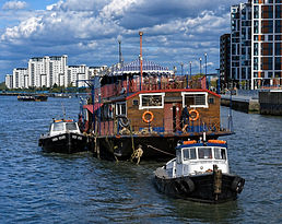 Regalia a large house boat with a striped canopy, flanked by two tugboats on a river.
