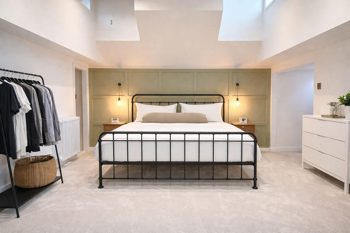 Modern bedroom with black metal bed, green accent wall, and skylights.