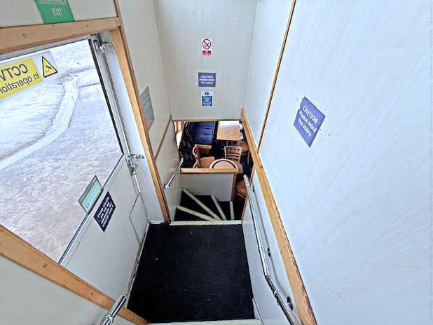 Narrow hallway leads down stairs, door with CCTV sign, safety notices.