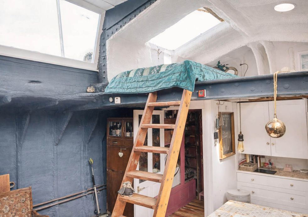 Cozy, rustic boat interior with a wooden ladder leading to a loft bed, kitchen area, and a large window.