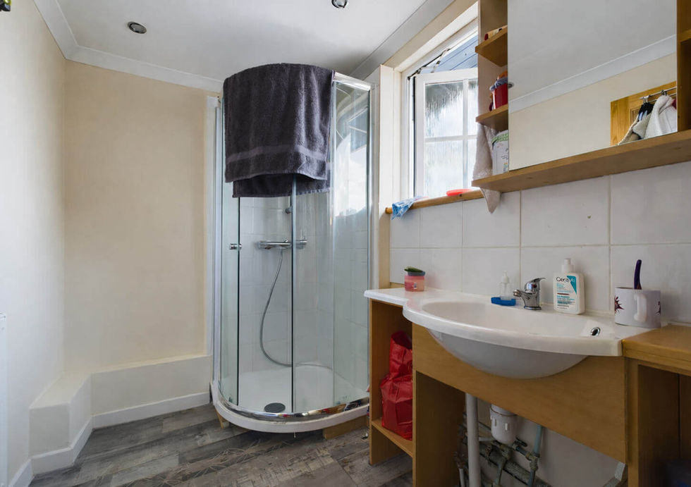 A modern bathroom with a glass shower, sink, and mirror. Towels and toiletries are neatly arranged on wooden shelves