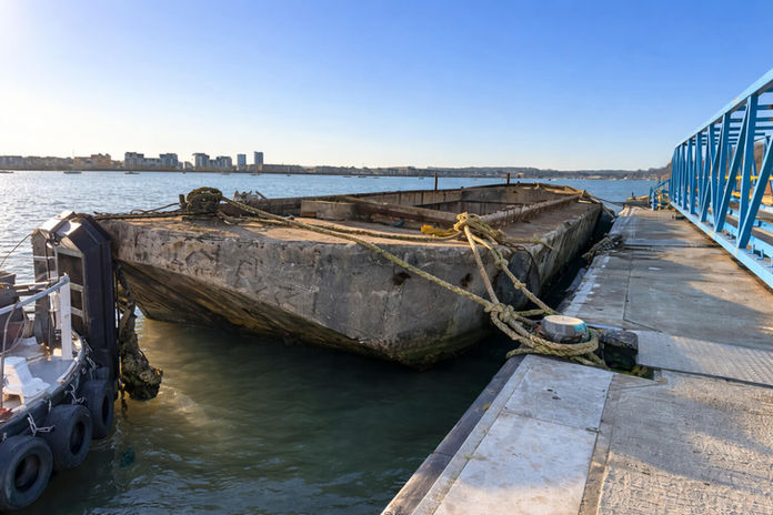 Concrete barge tied to a dock with blue railing on a sunny day.