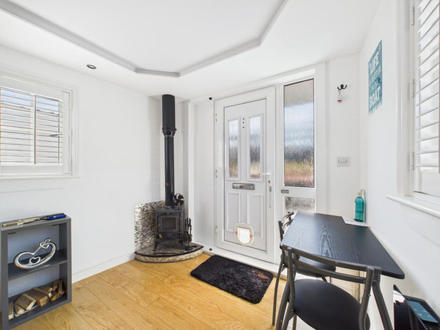 Cozy room with wood stove, white door, dining table, and window shutters.
